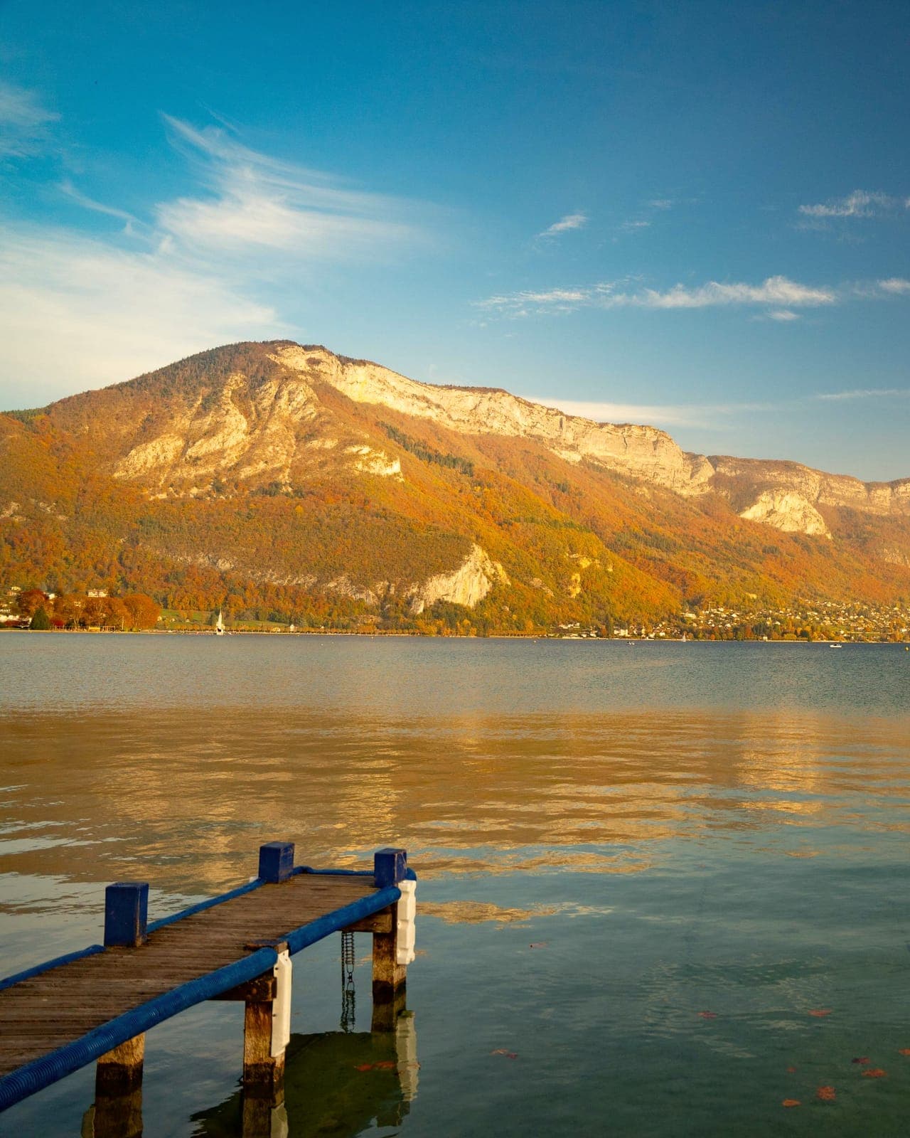 Le lac d'Annecy en automne, un ponton au premier plan et les montagnes dans une lumière de fin d'après-midi.
