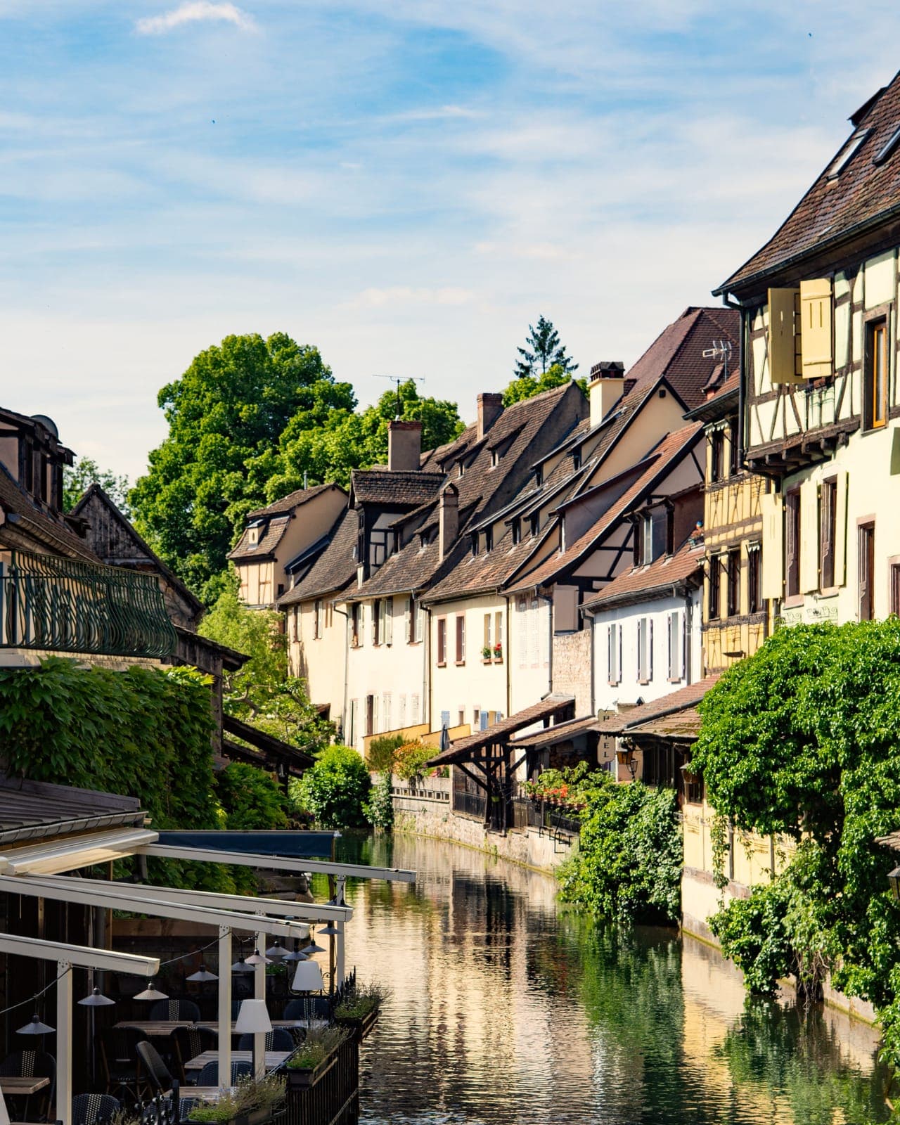 Un canal bordé de maisons à colombages et de verdure, à Colmar, par une journée d'été.
