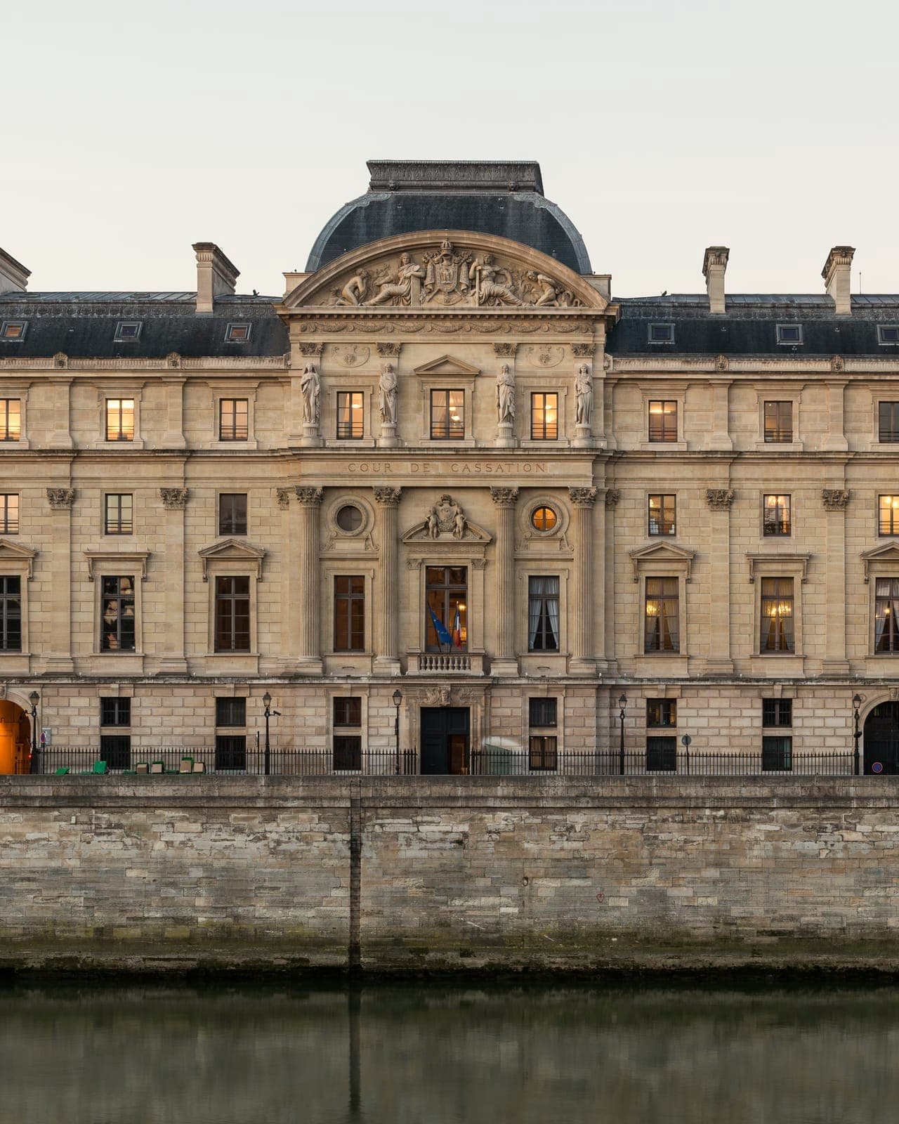 Façade classique en pierre claire d'un grand bâtiment à fronton sculpté et toit d'ardoise, au bord de la Seine, derrière un haut quai de pierre ; l'inscription « Cour de cassation » est gravée au centre.
