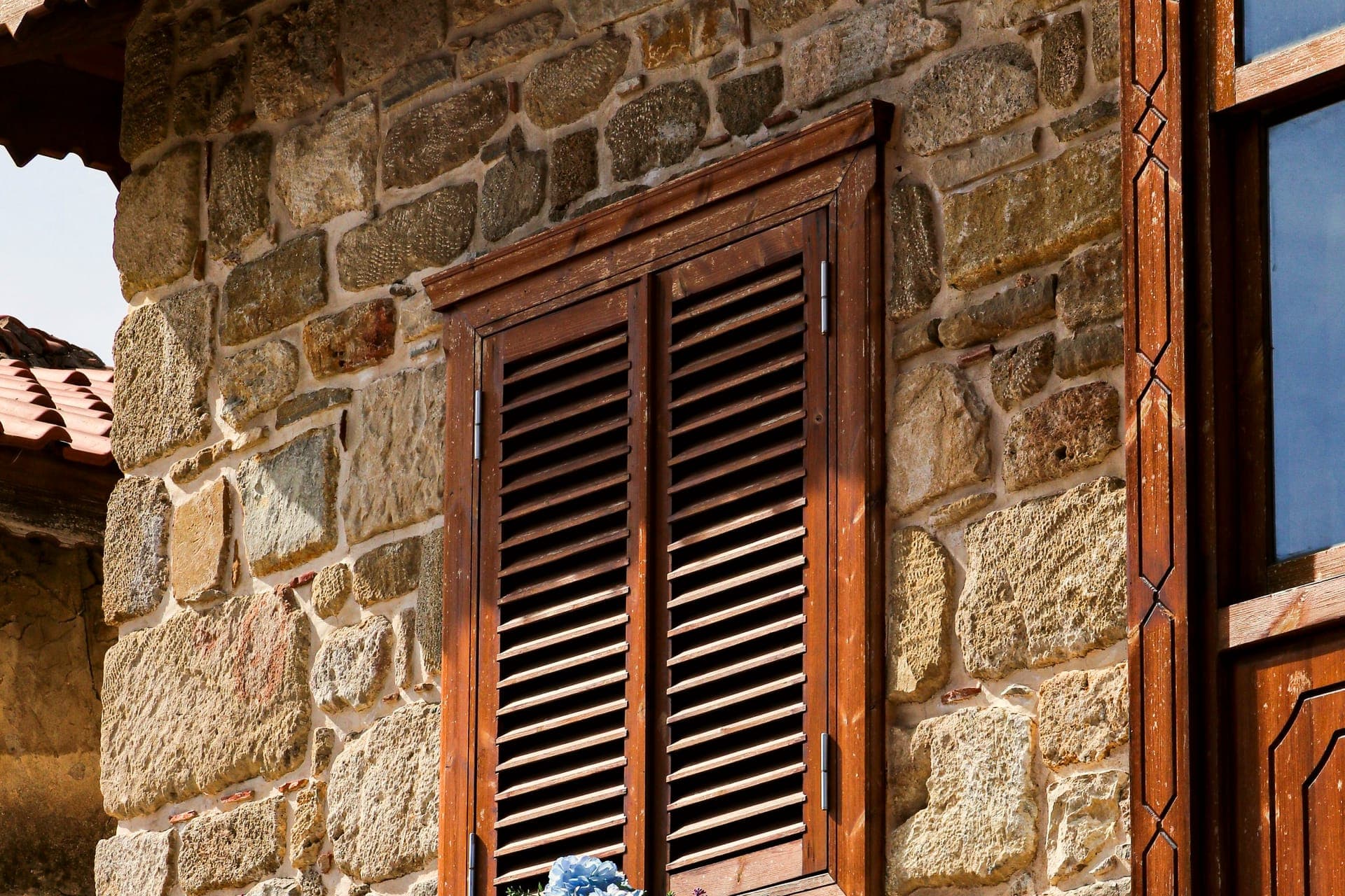 Façade d'une maison en pierre aux volets de bois, une jardinière fleurie sous la fenêtre.