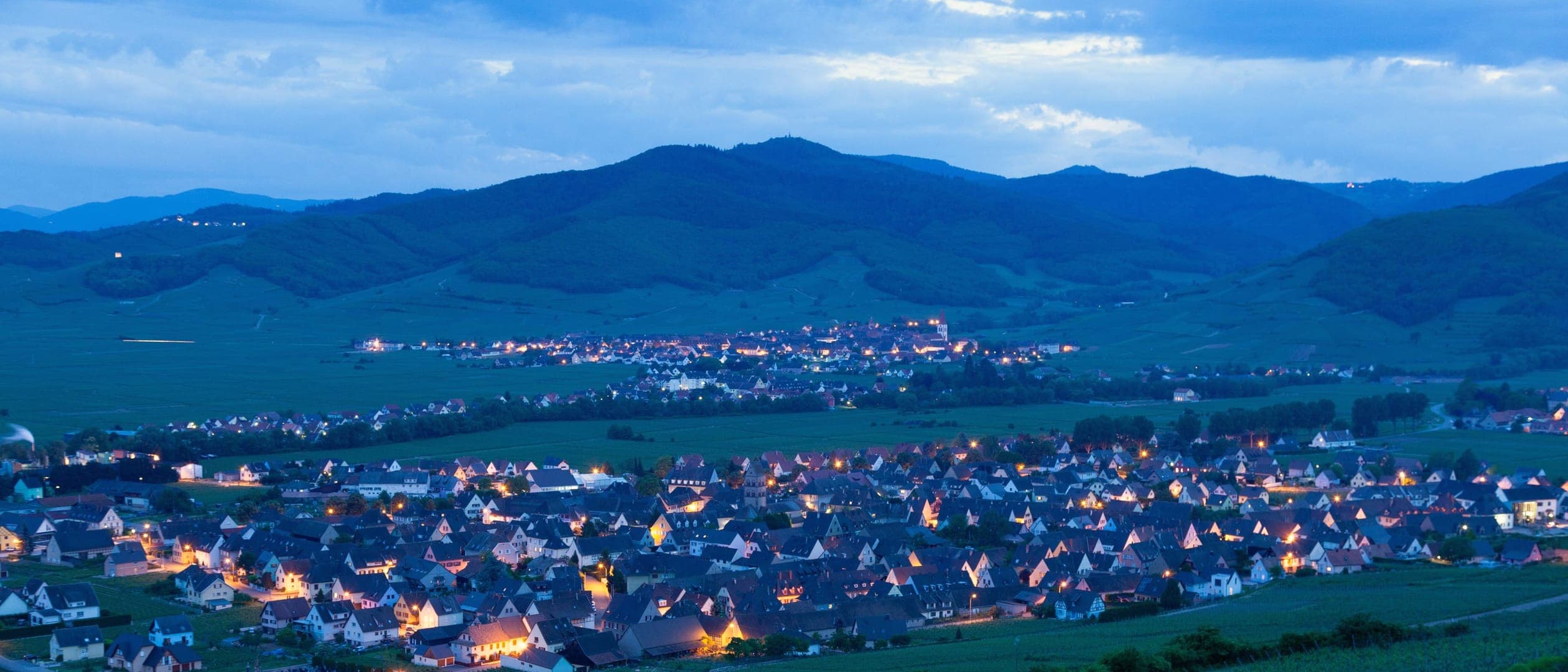 Les vignes et le village de Mittelwihr au soir, lumières allumées, au pied des Vosges.